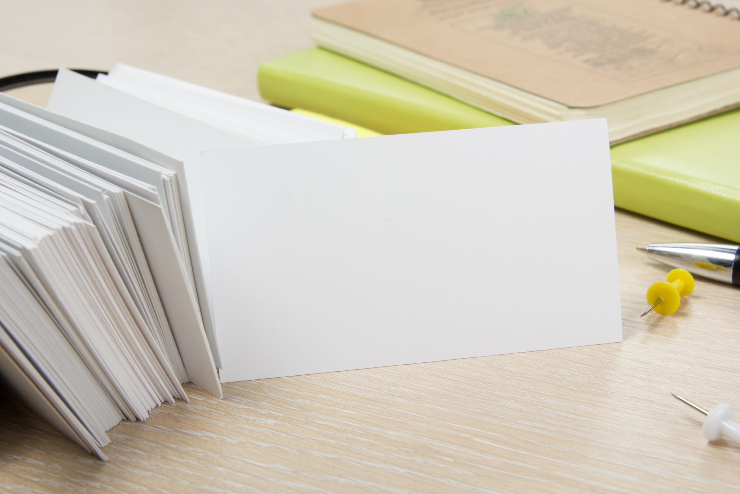 White blank business card. Office table desk with set of colorful supplies, cup, pen, pencils, flower, notes, cards on beige desk table background. Top view and copy space for ad text
